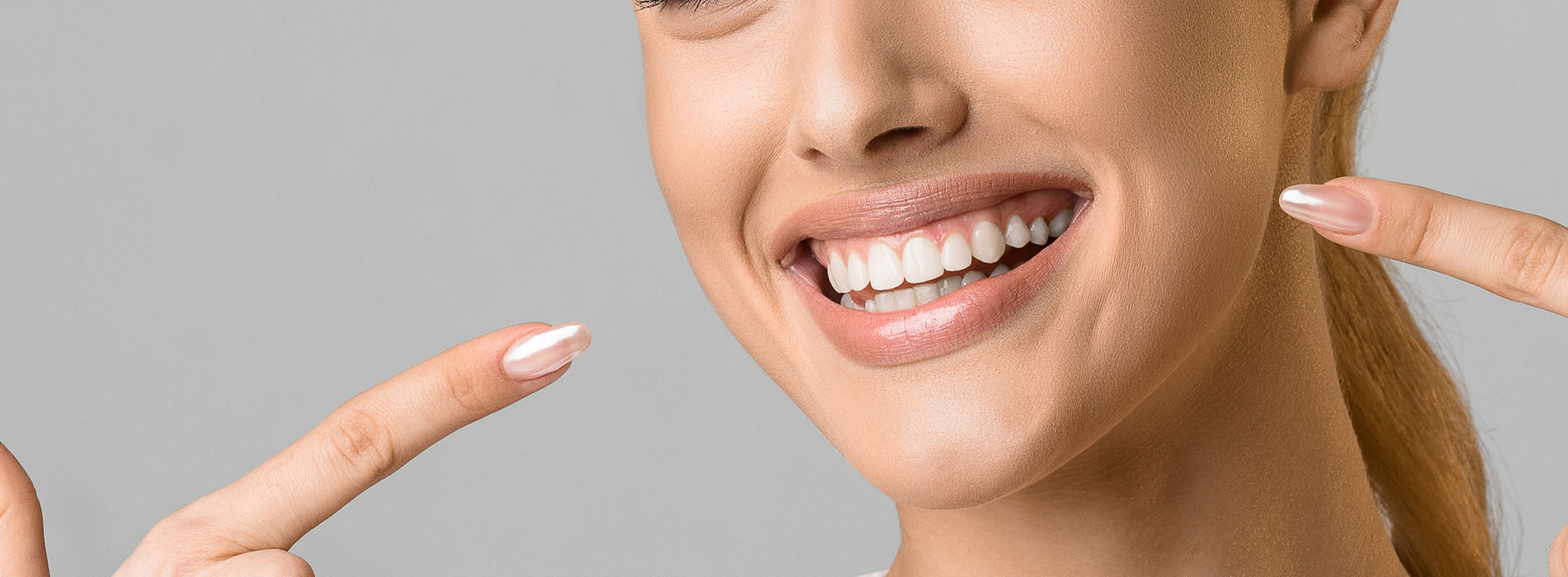 The image is a photograph of a woman with a radiant smile, showcasing her teeth and holding up two fingers near her face.